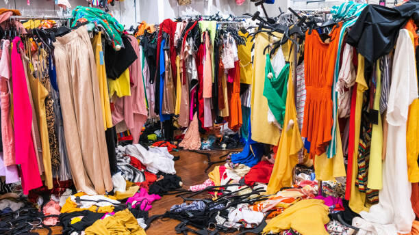 Chaos Racks of clothes with many clothing items strewn on the floor in a messs